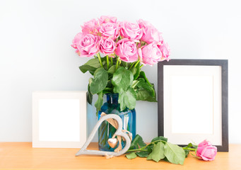 Violet fresh roses with heart and two empty photo frames on wooden shelf