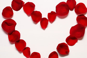 Heart of red rose petals on a white wooden background.