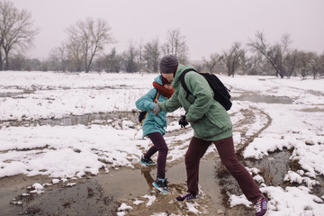 young woman and a man pass a puddle during the spring snow melt