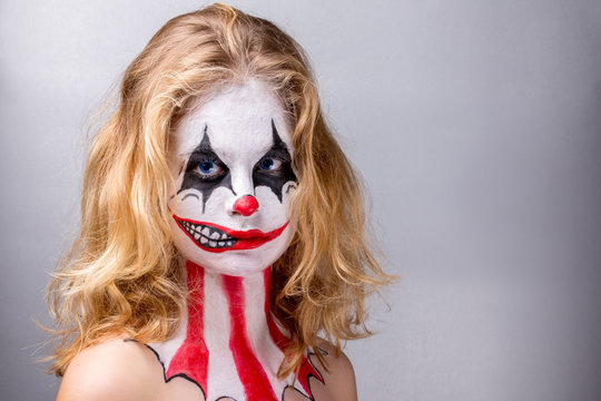 Portrait d'une jeune fille blonde maquillée en joker avec un faux sourire sur la moitié du visage