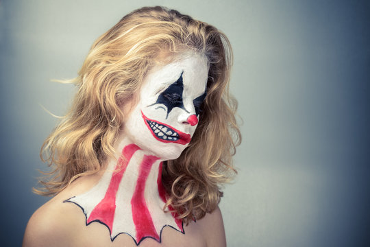 Portrait d'une jeune fille blonde maquillée en joker avec un faux sourire de profil, filtre vintage