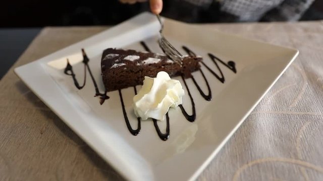 A typical Italian Neapolitan slice of Caprese cake made of chocolate and almonds with decorative melted chocolate and cream. Flat lay aerial view. Slow motion feeding.