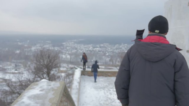 a Bearded Man and Two Young People at Artyom Monument Observation Deck With an Impressive View on Sviatogorskaya Lavra in Windy Weather in Winter
