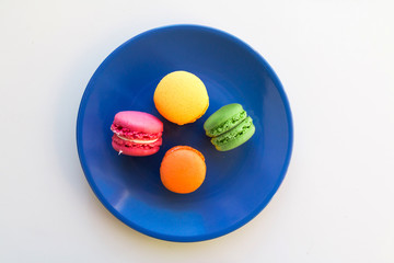 Yellow, orange, pink and green macaroons on blue round plate.