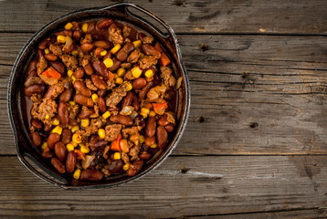 Traditional Mexican and Chilean dish of chilli con carne. In the rustic pan, next to tortillas and fresh vegetables on a wooden table, copy space