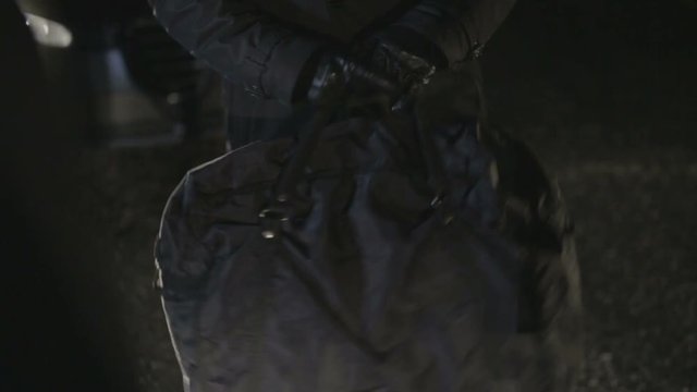 Criminale con i guanti neri che scambia la borsa di soldi in un parcheggio notturno