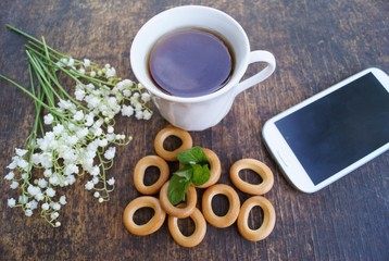 Bouquet of flowers and cup of tea on a wooden table with phone with a blank screen