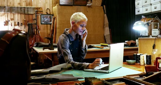 Craftswoman using laptop while talking on mobile phone