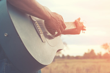 A man is playing guitar in grass field at relax day with sun light.