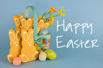 Cute gingerbread easter bunny cookies in a colorful basket with eggs and flowers on a blue...