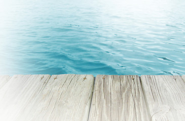 Background image of Inviting azure or cyan colored water as seen from the edge of a wooden boardwalk. Sun flare bouncing off water in distance. White vignette added.
