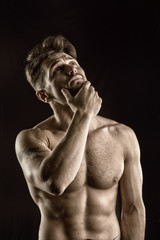 Handsome muscular, shirtless man looking up thinking with doubtful expression, isolated on black