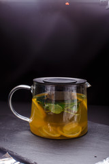 hot tea with mint and lemon in a glass pot on  black background