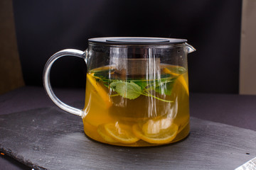 hot tea with mint and lemon in a glass pot on  black background