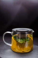 hot tea with mint and lemon in a glass pot on  black background