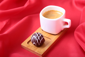 Coffee in white cup with chocolate pralines on red background
