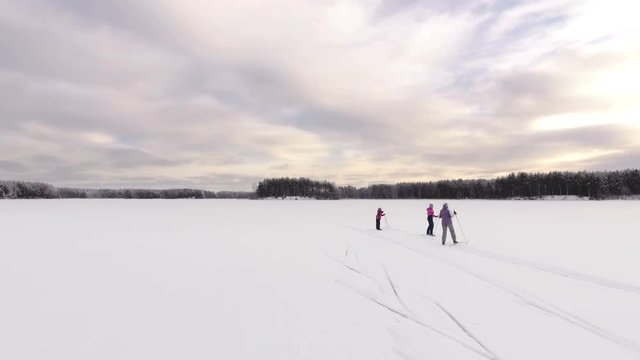 Top view at the two adult females and one child skiers walking skies on snowy ice of frozen forest lake. Waving hands