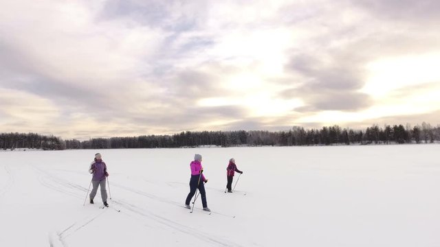 Three Caucasian skiers mature, young and small running cross-country ski on snowy ice of forest lake. Sunset at evening