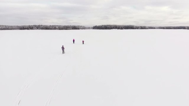 Two adult women and the child skiing on snowy white field of ice on lake, top view and rear view