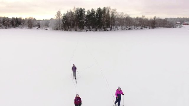 Family of three people playing sports, skiing on snow-covered frozen lake in the village