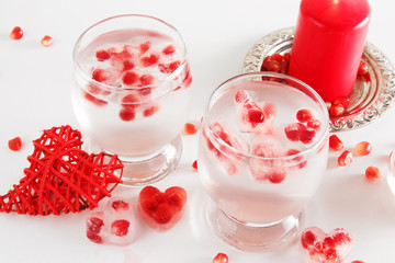 Romantic still life. Two glasses with alcoholic cocktail and ice, decorated with pomegranate, red candle, handmade heart, jelly candies, confetti. Saint valentine's day celebration.