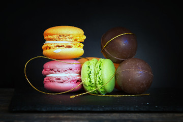 Yellow, orange and green macaroons and chocolate balls on slate against black background with golden decorative details - valentines day concept.