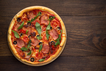 Italian pizza with ham, tomatoes, olives, cheese and herbs on vintage wooden background.