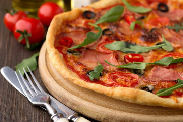 Homemade pizza with ham, cheese and vegetables on wooden table.
