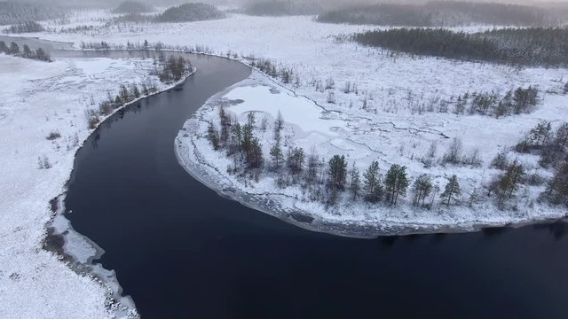 Black water river bend is in white snow covered swamps of Karelia. Aerial view from flying drone. Russia
