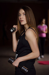 Fototapeta na wymiar Photo of beautiful young woman with long hair and dumbbells at the gym. Fitness concept