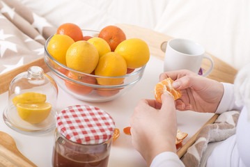 Close up of hands peels tangerines with citrus fruits and honey served on wooden tray.