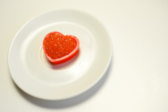 Red caviar in a heart shape on white plate background