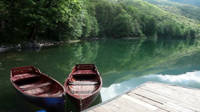 Kayaks; canoes and wooden rowboats are near planked pier in Biogradskoe lake. Calm and beautiful water with green lush on shores. Biogradska Gora national park. Montenegro
