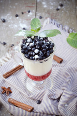 Delicious parfait dessert with bilberry berries, milk souffle and jello layers. Frozen treat in a glass on a rustic wooden background