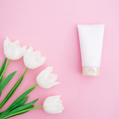 Floral bouquet with white flowers, cosmetics, face cream on pink background. Flat lay, top view.