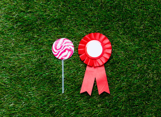 Red reward and lollipop on green grass background