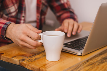 Young handsome man drinking tea and looking at laptop screen