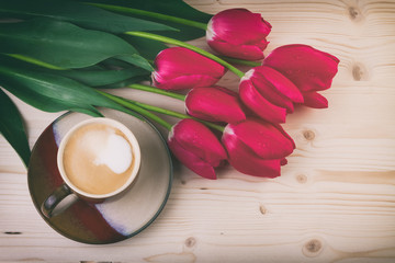Cup of coffee with spring flowers red tulips on wooden table. Vintage style