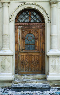 Antique classic pastel marble facade with rough rustic sculptured wooden door and old monochrome stained glass. Vertical image.
