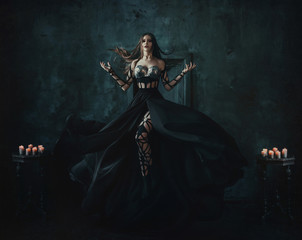 Beautiful witch floating in the air. Background dark room. Girl dressed in a black dress with a...
