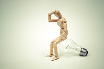 Wood Figure Mannequin sit on incandescent light bulb and think  