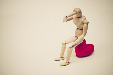 Wood Figure Mannequin sitting sadly on a red heart waiting for love
