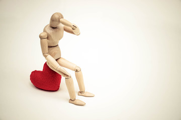 Wood Figure Mannequin sitting sadly on a red heart waiting for love