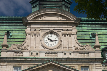 Fototapeta na wymiar Clock of City Hall in Old Montreal, Quebec, Canada. Mansard roof, fleur de lis, and rounded pediment architectural details of New French Imperialism architecture.