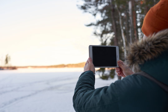Man in hipster clothes keep tablet outdoor in winter time. Guy make snapshot of snow contryside. Talking with help of internet technology in the forest. Travel concept with free space of advertising.