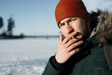 Smoking man outdoor with winter field and forest background. Guy look to the camera with a...