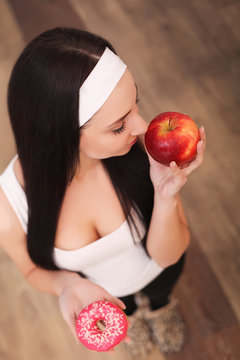 Diet. Dieting concept. Healthy Food. Beautiful Young Woman choosing between Fruits and Sweets