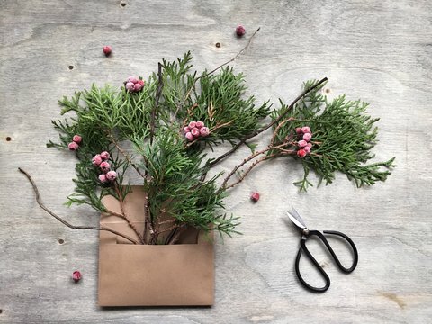 Overhead view of an open brown envelope with fir branches, frosted berries and a pair of scissors on a wooden table