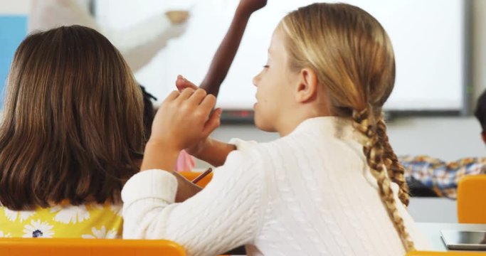 Schoolgirl whispering into her friends ear in classroom