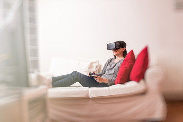 Fototapeta premium Young woman sitting on the sofa at home having fun playing a vir